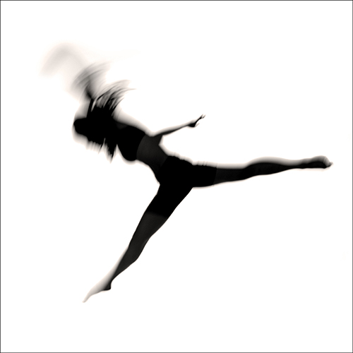 A blurred silhouette of a person captured mid-air, gracefully leaping with one leg extended forward and the other backward. The background is a soft white, emphasizing the motion and fluidity of the jump.