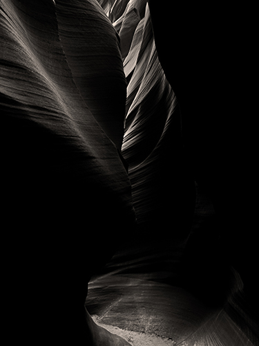 Light subtly illuminates parts of a slot canyon, creating a play of light and shadow, emphasizing the texture and curves.