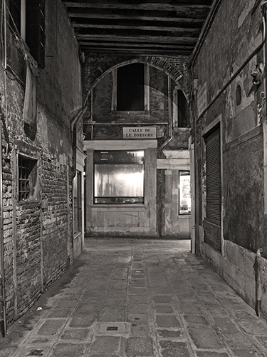 A deserted covered alleyway at night in Venice, Italy with cobblestoned floor and arched opening.