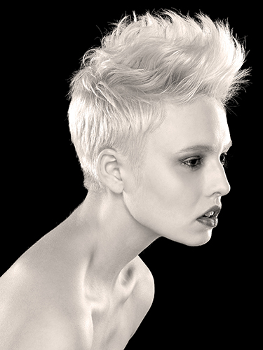 Black and white image of a woman with short, textured hair styled upwards. She has a focused expression and is gazing to the side against a plain, dark background