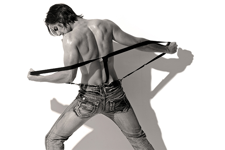 A shirtless person facing away, wearing jeans and holding suspenders.