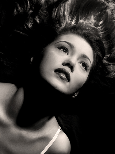 A black and white portrait of a woman with long hair spread out, gazing upward. The image is reminiscent of vintage Hollywood glamour.